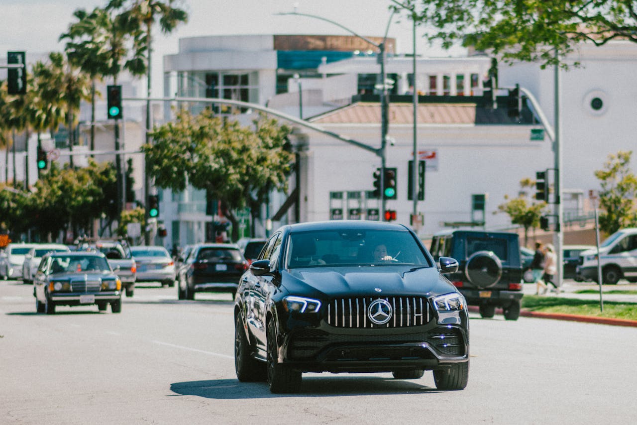 A black luxury Mercedes driving on a bustling city street on a bright day.