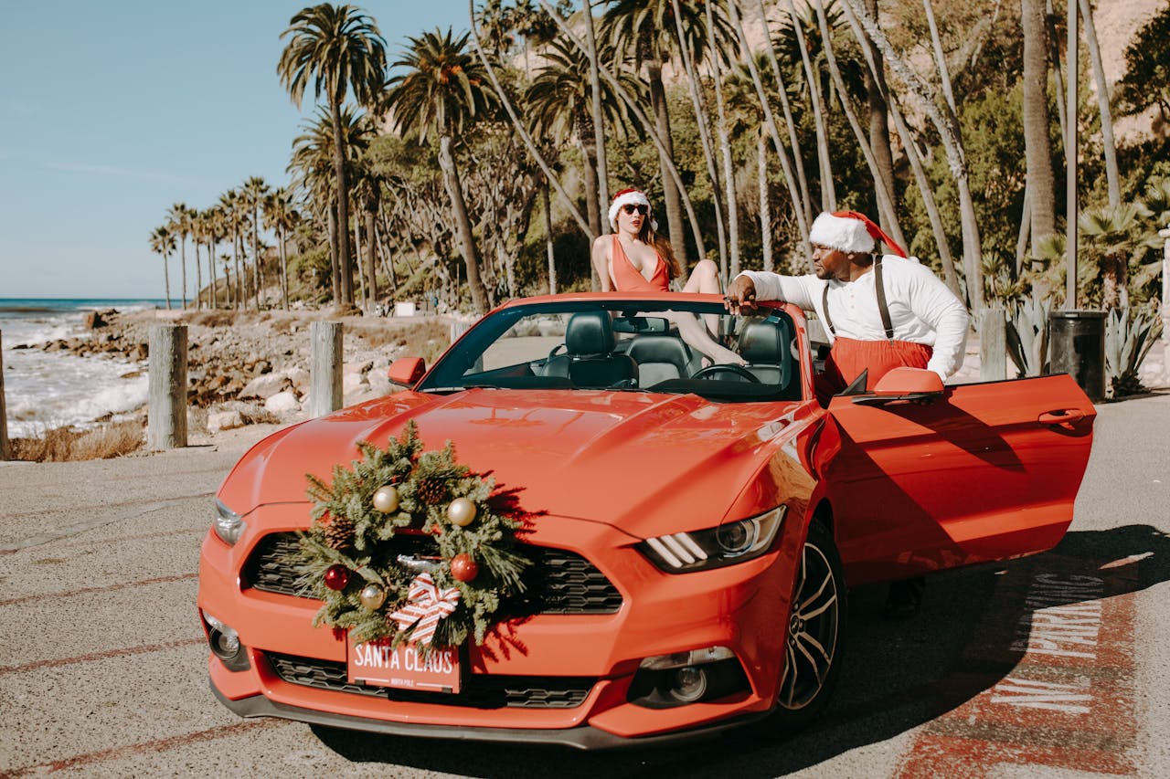 Santa and a holiday companion enjoy a convertible by the beach with a festive vibe.
