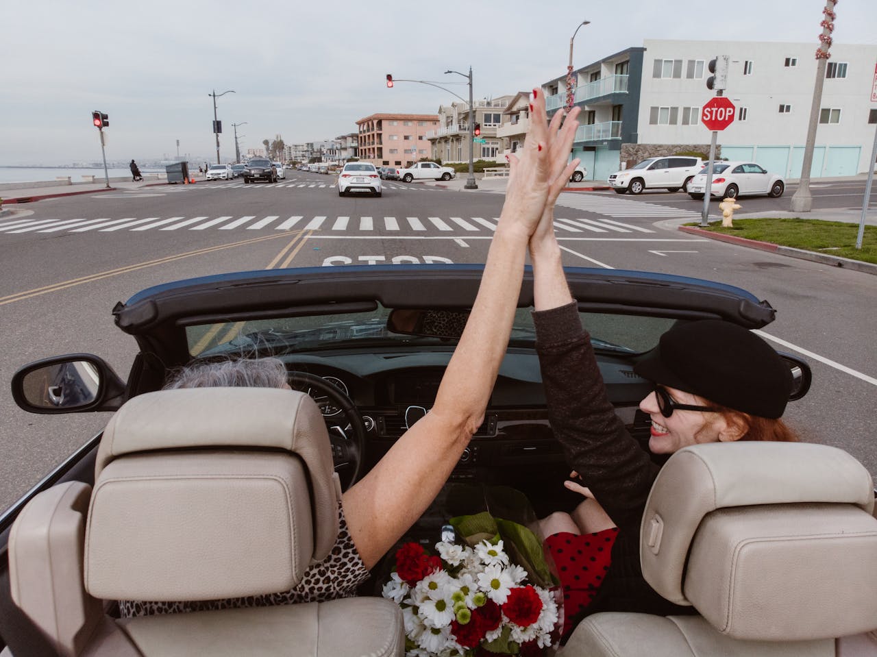 Two women high-fiving in a convertible on a scenic drive in Redondo Beach, CA.