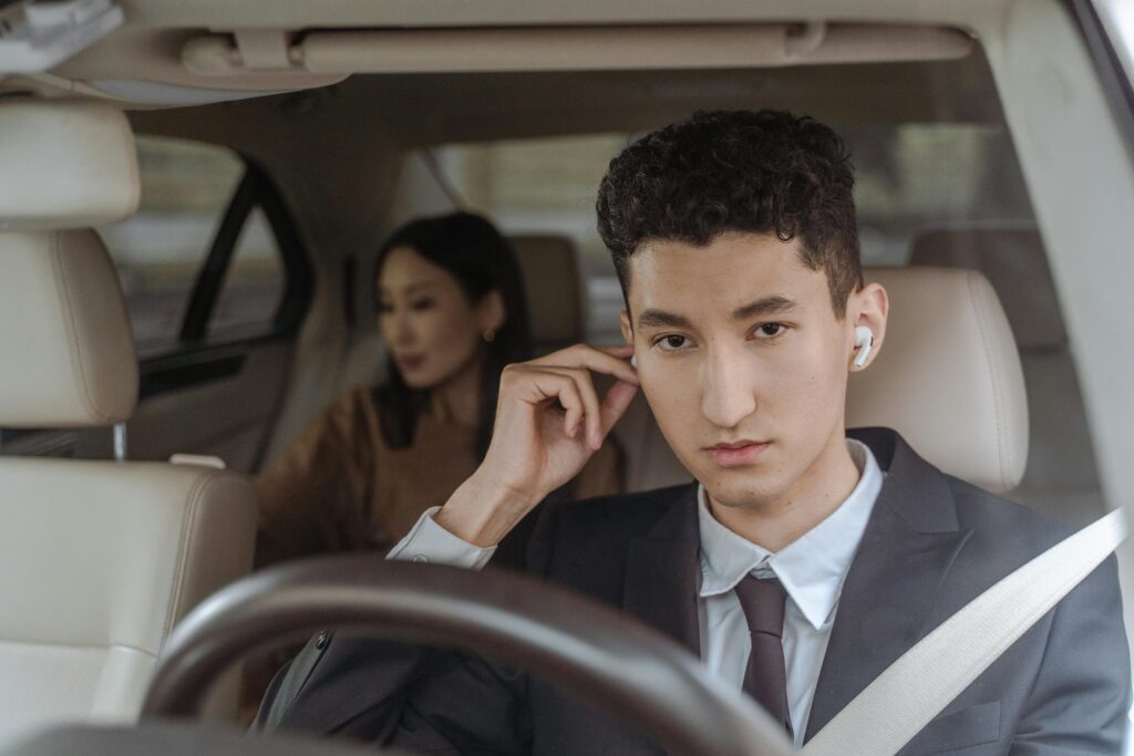 A professional driver in a suit with AirPods driving a female passenger in a car.